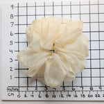 Load image into Gallery viewer, A cream-colored sheer pure silk organza ruffled hair scrunchie placed on a white background with a black grid ruler showing inches and centimeters for scale.
