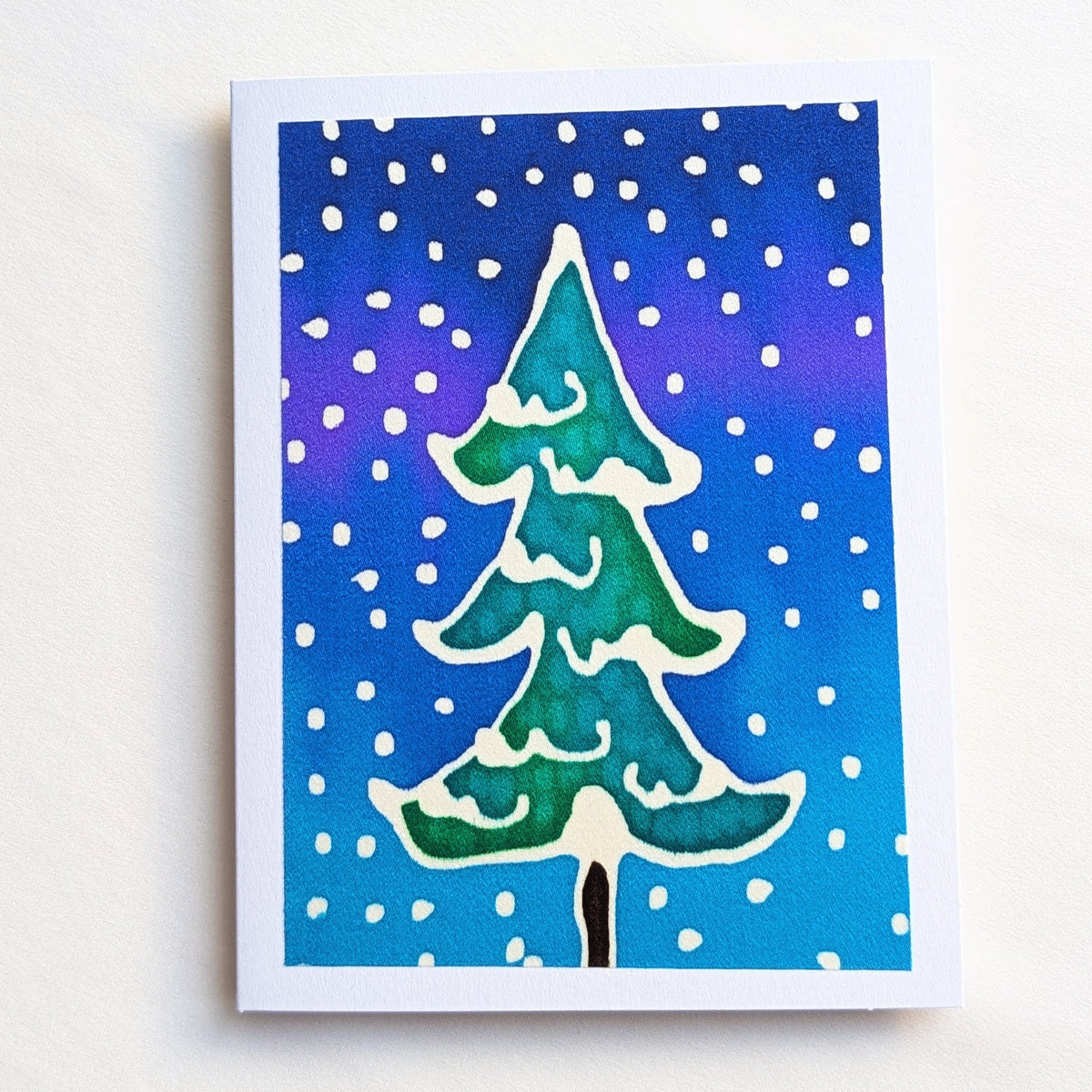 hand painted pure silk original art greeting card featuring a hand-painted green Christmas tree with white snow details against a blue and purple gradient background with white snow dots,