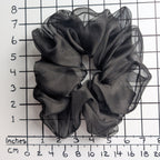A  pure silk jumbo oversized black sheer organza hair scrunchie displayed on a white background with a black grid ruler showing inch measurements.