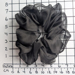 Load image into Gallery viewer, A  pure silk jumbo oversized black sheer organza hair scrunchie displayed on a white background with a black grid ruler showing inch measurements.
