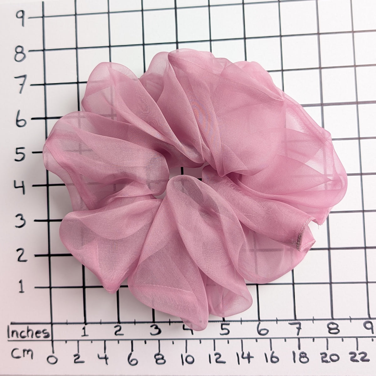 A dusty pink pure silk organza oversized jumbo sheer  scrunchie laid flat on a white background with a black grid ruler showing inch measurements.