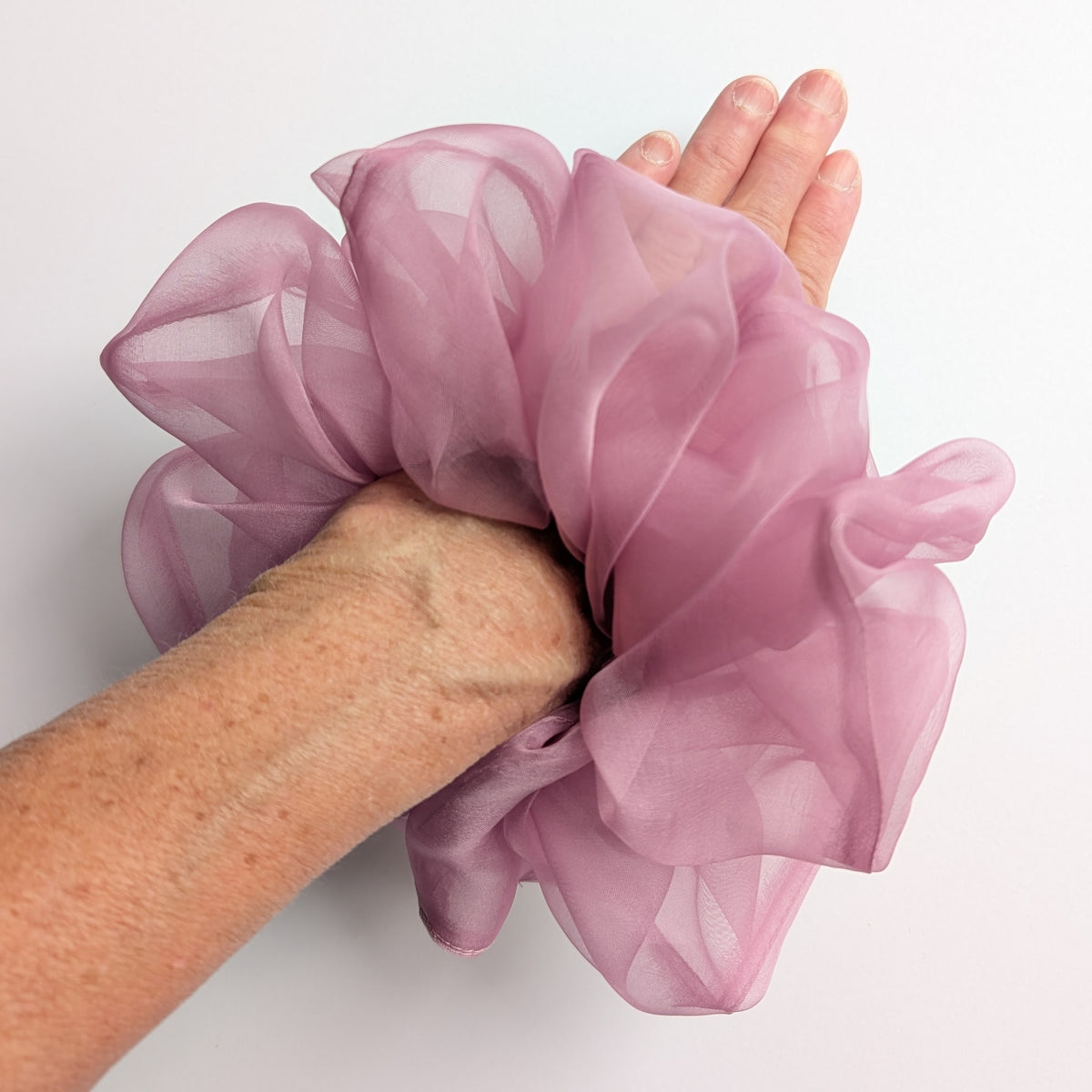 A dusty pink pure silk organza oversized jumbo  sheer  scrunchie worn on a person's wrist, 