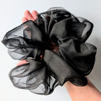 A large black sheer pure silk organza hair scrunchie held up by a hand  
