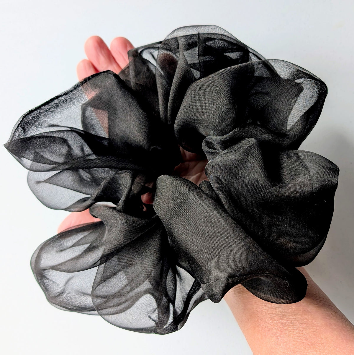 A large black sheer pure silk organza hair scrunchie held up by a hand  