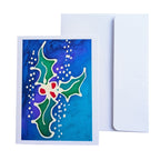 A hand painted pure silk original art  greeting card with a colorful holly design on a blue watercolor background, shown in front of a plain white envelope