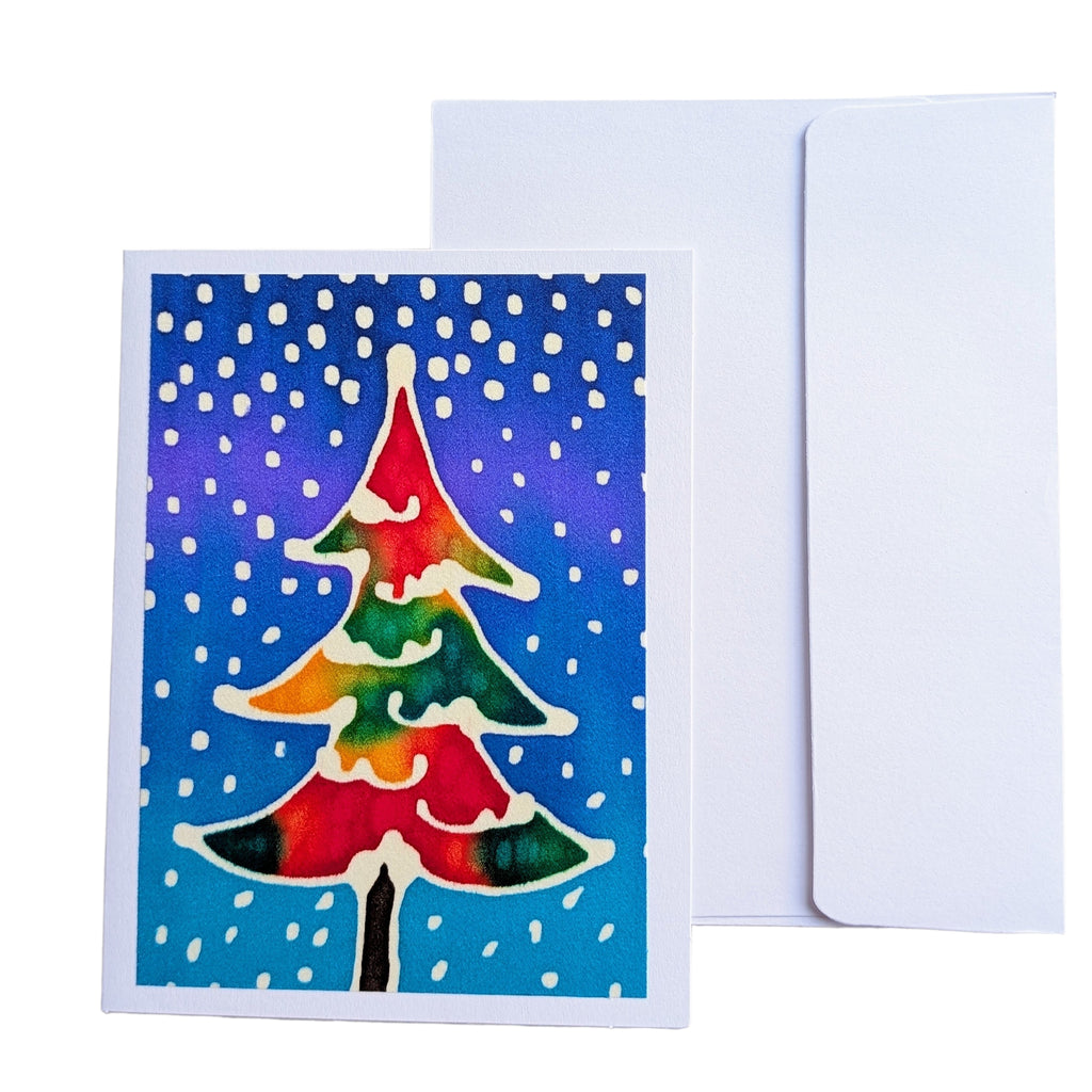 A hand painted pure silk original art cardgreeting card with a colorful watercolor Christmas tree on a blue snowy background, shown in front of a plain white envelope 