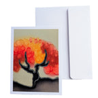 A hand painted pure silk original  greeting card with a colorful abstract tree design in red, orange, and yellow tones, shown in front of a plain white envelope 