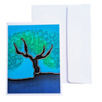 A hand painted  pure silk art card  greeting card with a stylized tree illustration in blue, green, black, and dark blue, shown in front of a plain white envelope 